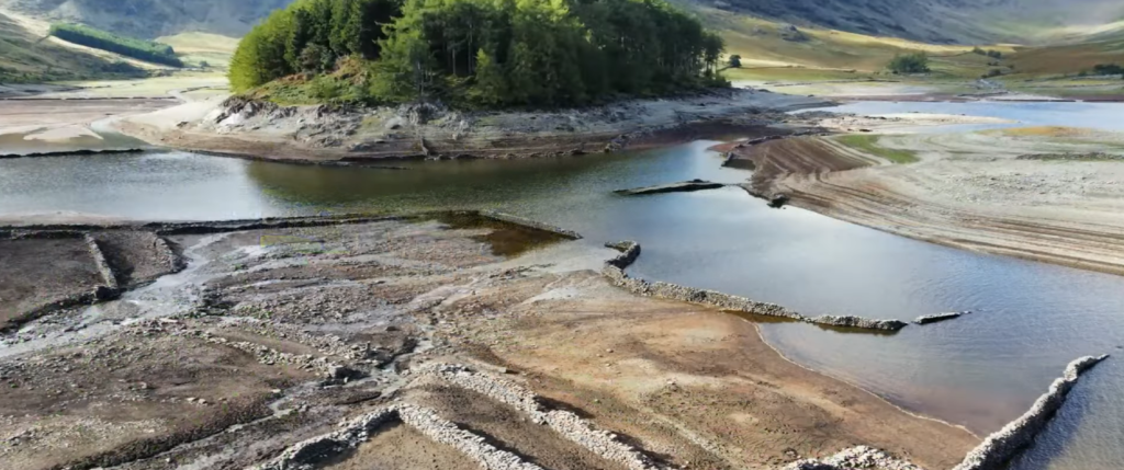 Serene landscape with exposed lakebed, water inlets, and distant green hills